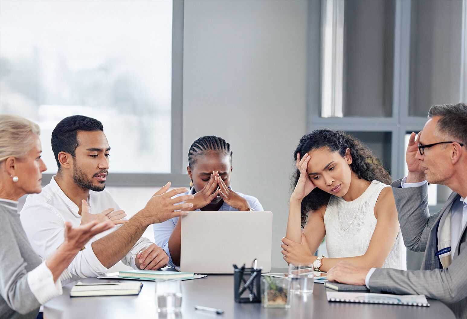 A group of professionals seated at a table appear stressed and concerned.